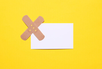 White business card with medical plaster on yellow background