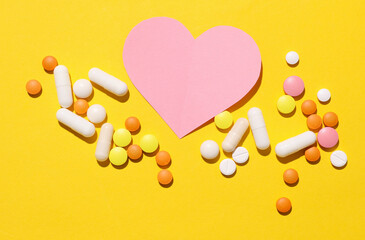 Paper heart and pills on yellow background. Medicine concept. Heart disease treatment