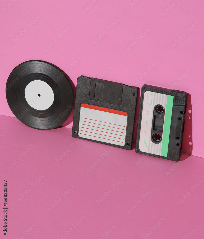 Poster outdated technologies. retro 80s audio cassette with floppy disk and vinyl record on pink background