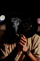Mysterious Silhouette: A person, shrouded in shadows, holds a lit cigarette, the curling smoke...
