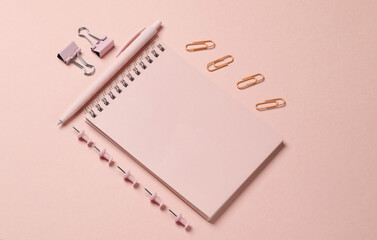 Pink stationery accessories on a pink background. Notepad, pen, paper clips, pins. Monochrome...