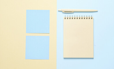 Notebook with memo papers, pen on a blue-yellow pastel background. Creative layout