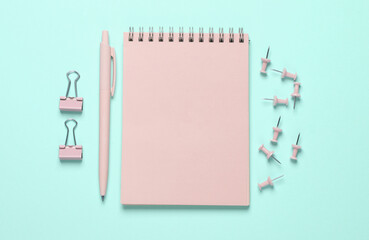 Pink stationery accessories on blue background. Notepad, pen, paper clips, pins. Flat lay. Top view