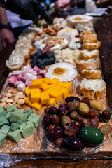 Close-up of assorted cheese cubes, mixed olives, nuts, and sliced bread on a rustic wooden board. Perfect snack or appetizer for party, wine tasting, or family dinner.