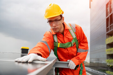 A man in a yellow hard hat and orange safety suit is working on a roof