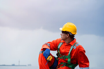 A man in a yellow helmet and orange jumpsuit is sitting on the ground