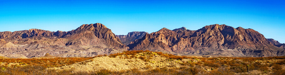 Panoramic view of rugged desert mountains in Big Bend National Park under a bright blue sky. Layers of geologic formations create dramatic contrast across this remote, scenic landscape.