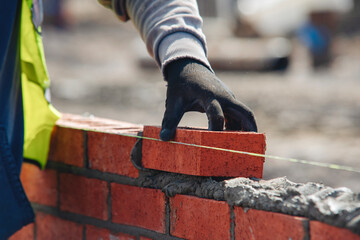 Bricklayer constructing stone wall using bricks, cement mortar mix and trowel