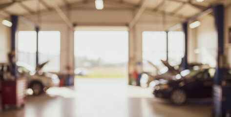 Blurred interior of a garage with cars being repaired and an open door.