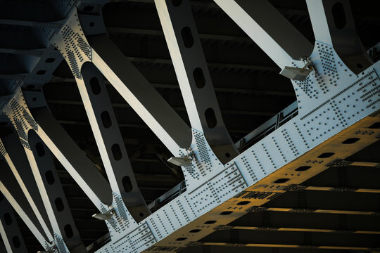 Close-up view of a steel bridge structure featuring diagonal support beams, industrial rivets, and geometric patterns. Urban architecture and engineering concept