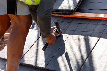 Builder carefully places roof tiles on a sloped surface while standing on top of a building...