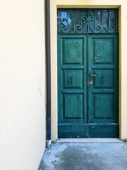 Old wooden door with green paint and white wall in the background.