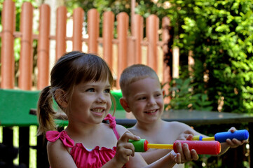 Happy children playing with colorful water blasters outdoors in a summer backyard. 