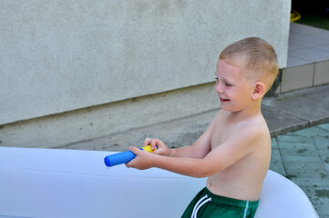 A little boy in a green swim trunks is playing with a water gun in the pool.
