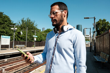 Young businessman using smartphone while waiting for train at station