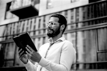 Bearded businessman reading a book in urban setting, analog style monochrome photography