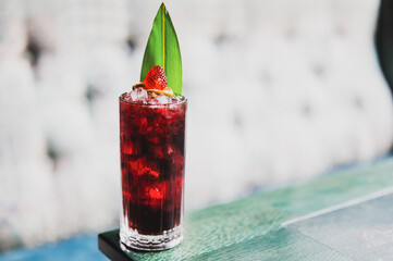 Refreshing red cocktail with ice, strawberry, citrus slices, and mint leaf in a tall glass on a...