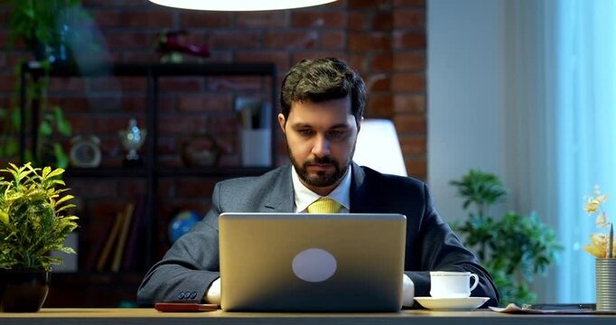 Businessman drafting email or typing on laptop sitting at office desk, Indian Asian corporate executive focused on communication, digital work, online correspondence, modern business productivity