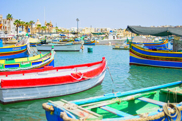 Obraz premium Malta Republic, Malta Island. 25.05.2023. Marsaxlokk city, The harbour and brightly coloured traditional boats on a hot sunny day.