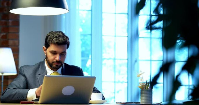 Businessman drafting email or typing on laptop sitting at office desk, Indian Asian corporate executive focused on communication, digital work, online correspondence, modern business productivity