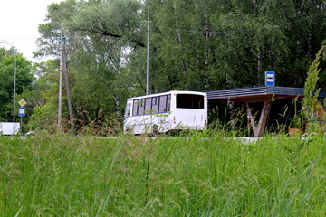 There is a white bus parked at the bus stop on the highway.