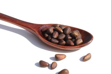 On a white background lies a wooden spoon with pine nuts.