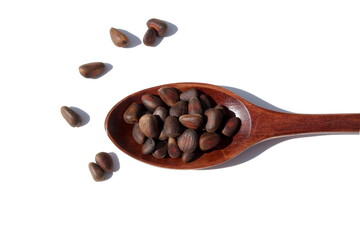 On a white background lies a wooden spoon with pine nuts.