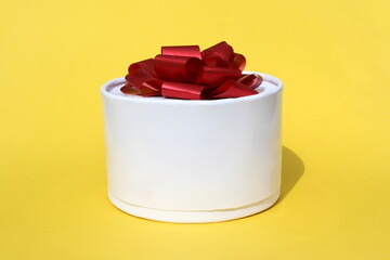 On a yellow background there is a round white gift box with a bow.