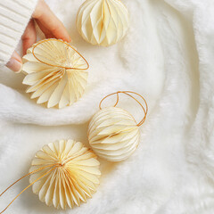 New Year Festive winter holidays concept, Minimal style top view aesthetic layout with hand holding cream beige paper ornaments, Christmas balls on white fluffy fur background, creative flat lay
