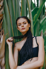Attractive woman in black swimsuit posing by palm tree against lush green backdrop
