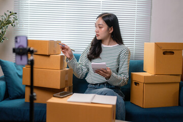 Young entrepreneur woman is holding calculator and checking parcels, recording video live streaming...