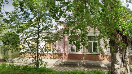 Old pink brick building surrounded by trees. Small stone house in garden. Young spring bright greenery of trees