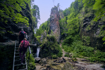 Hikers ascend ladders in a rugged gorge with a distinctive rock formation. © Miro
