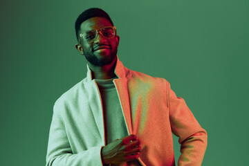 A stylish African American man exuding confidence in a light coat against a vibrant green backdrop,...