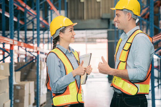 Confidence caucasian man, woman staff worker wear safety helmets, vest show teamwork collaborate, cooperation in logistics inventory operation. show success, efficiency in modern warehouse management.