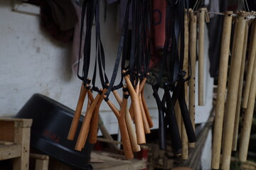Wooden slingshots with black rubber bands hang from hooks. Bamboo sticks, cloths, and a black...