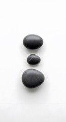 Three Smooth, Dark Gray Spa Stones Elegantly Arranged on a Pristine White Background, Symbolizing Balance, Serenity, and a Harmonious Approach to Wellness and Inner Peace.