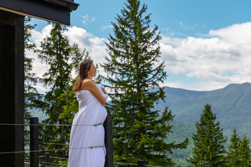 Pregnant woman enjoying mountain morning view. A pregnant woman wrapped in a white blanket stands...
