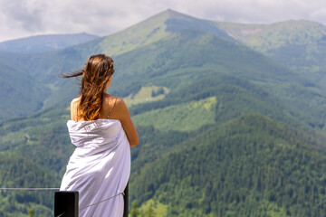 Woman wrapped in blanket overlooking mountains. A woman with windblown hair stands wrapped in a...