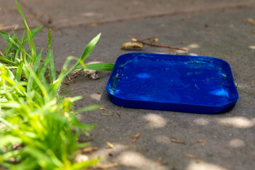 Bright blue tray rests on sunlit concrete surrounded by lush green grass on a warm summer afternoon
