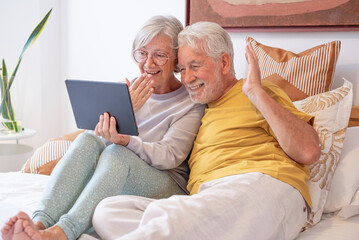 Happy senior family couple bonding embracing at bedroom at home or hotel room enjoying tech and social with digital tablet. Love and relationship people indoor