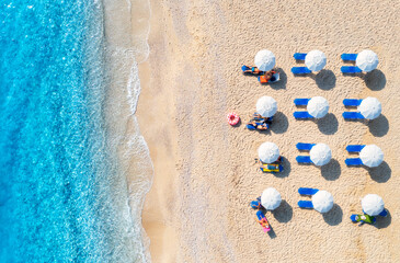 Aerial view of tourists relaxing on sunbeds under umbrellas on a beautiful sandy beach with...