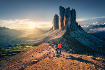 Female hiker enjoying the breathtaking sunrise over the Tre Cime di Lavaredo, three striking peaks rising majestically in the Dolomites, Italy. Landscape with woman, trail, rocks. Trekking and hiking © den-belitsky