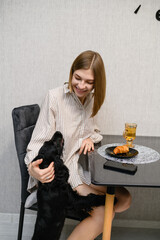 Smiling woman cuddling black cocker spaniel puppy at breakfast table.