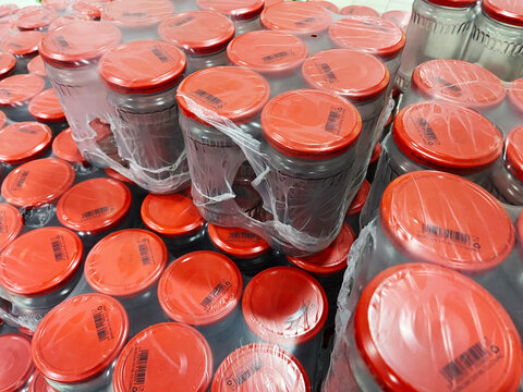 Large quantity of glass jars with red lids, some shrink-wrapped in bulk, perfect for food packaging, preservation, or commercial storage and distribution designs