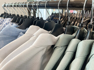 A neat row of men's button-down shirts in various light colors and patterns, including blue, white,...