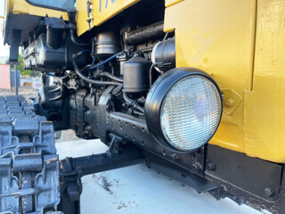 Close-up view of a yellow industrial bulldozer with visible tracks, headlight, and engine components, showcasing rugged construction equipment used for heavy-duty tasks and earthmoving operations. © Bolucevschi