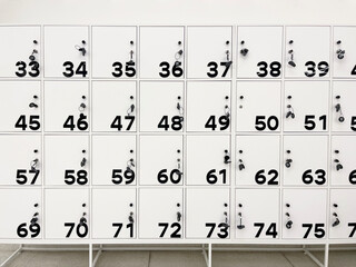 Minimalist white locker wall with black numbered doors and keys inserted, ideal for storage in...