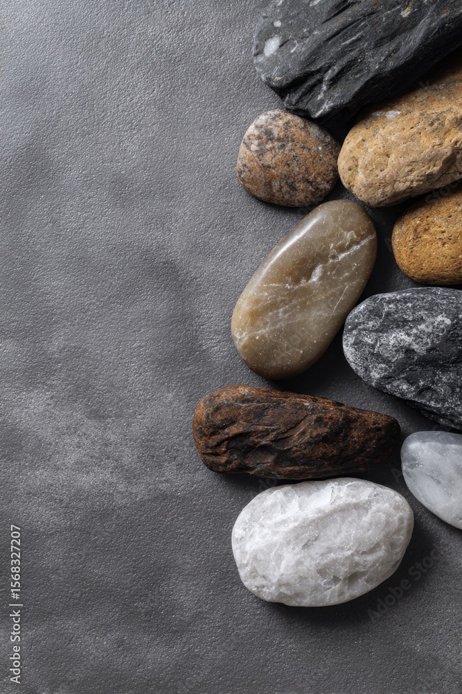 Poster overhead view of collection of smooth rocks arranged along right edge of grey textured background.