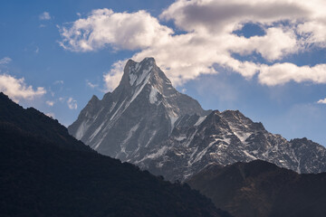A breathtaking view of the snow-capped peak of Machapuchare when the clouds softly hug the mountains in great Himalayas in Nepal.